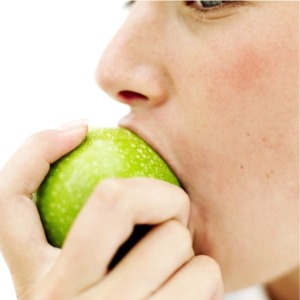 Woman taking bite of green apple.